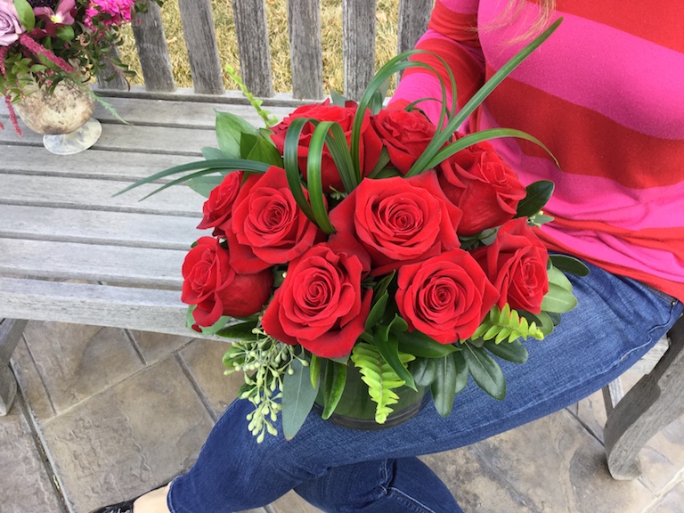 Roses arranged in a clear cylinder with bear grass shaped like a heart