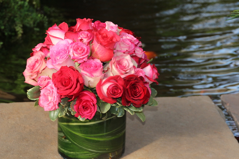 Mixed red and pink roses in a glass cylinder lined with greens